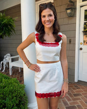 Load image into Gallery viewer, Woman in a white dress with red accents standing on a porch.