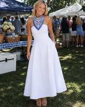 Load image into Gallery viewer, A woman stands outdoors at a market wearing a sleeveless white maxi dress with a blue patterned scarf and tan sandals.