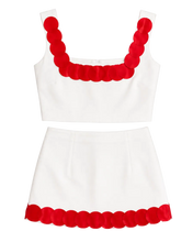 Load image into Gallery viewer, A white two-piece outfit set consisting of a sleeveless crop top and a matching mini skirt, both featuring a bold red scalloped trim along the neckline and hem.