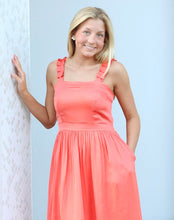 Load image into Gallery viewer, Woman in a coral dress standing against a white wall.
