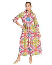Load image into Gallery viewer, A woman modeling a long-sleeved collared shirt dress with a vibrant geometric and floral pattern in yellow, pink, blue, and green, paired with beige heels against a plain white studio background.